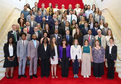A group of gardaute students and administrators pose on a marble staircase with a red carpet.