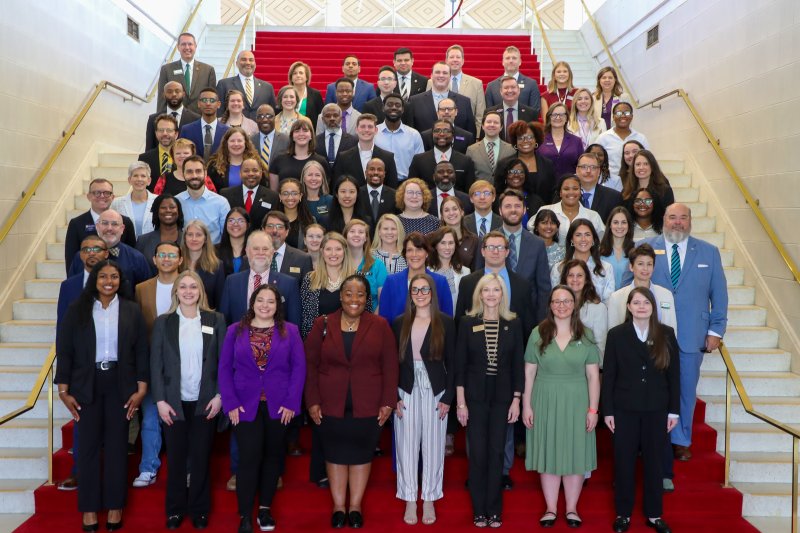 A group of gardaute students and administrators pose on a marble staircase with a red carpet.